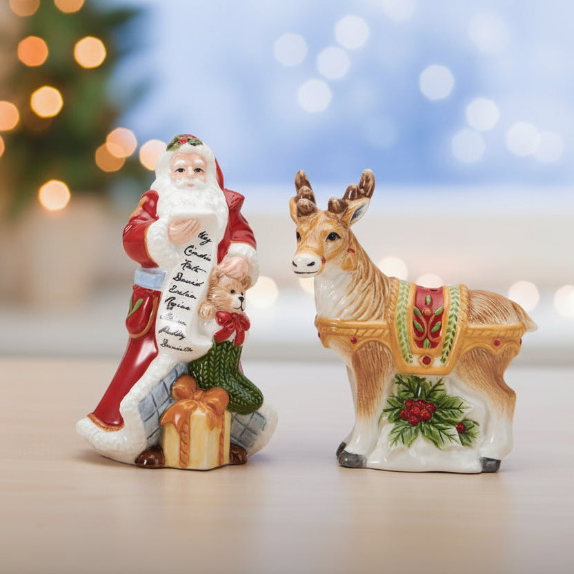 Two Christmas figurines on a tabletop: Santa Claus holding a sack and list, next to a decorated deer with a small candle inside, against a softly blurred holiday background.
